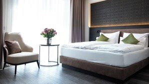 A modern hotel room with a large bed, a chair, and a small table with a vase of flowers. - in2 The Boardinghouse (Uebach-Palenberg)