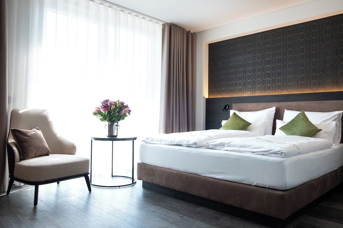 A modern hotel room with a large bed, a chair, and a small table with a vase of flowers.