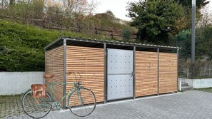 A small wooden structure with a metal door, possibly a storage shed or utility room, next to a bicycle on a paved area. - in2 The Boardinghouse (Uebach-Palenberg)