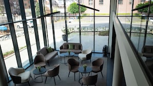 A modern indoor seating area with sofas and chairs arranged around small tables, large windows offering a view of the street and parked cars outside. - in2 The Boardinghouse (Uebach-Palenberg)