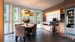 A modern kitchen with a built-in refrigerator, a dining area with a round table and chairs, and large windows providing natural light. - in2 The Boardinghouse (Uebach-Palenberg)