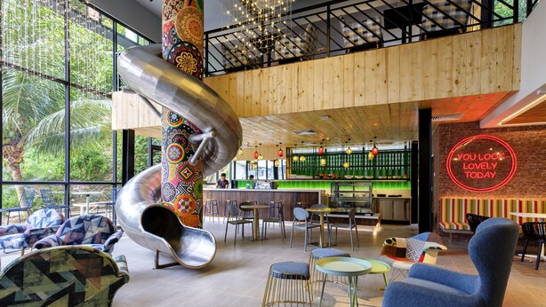 A modern interior with a central spiral slide, seating areas, and a neon sign. - TOOJOU Kota Kinabalu - Travel Meets Social (Kota Kinabalu)