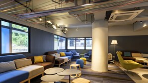 A modern lounge area with sofas, chairs, and tables, featuring large windows and a ceiling with exposed ductwork. - TOOJOU Kota Kinabalu - Travel Meets Social (Kota Kinabalu)