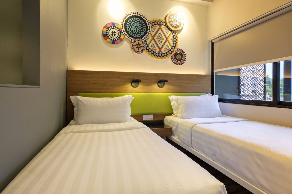 A hotel room with two beds, a decorative wall with circular patterns, and a window with a view of buildings.