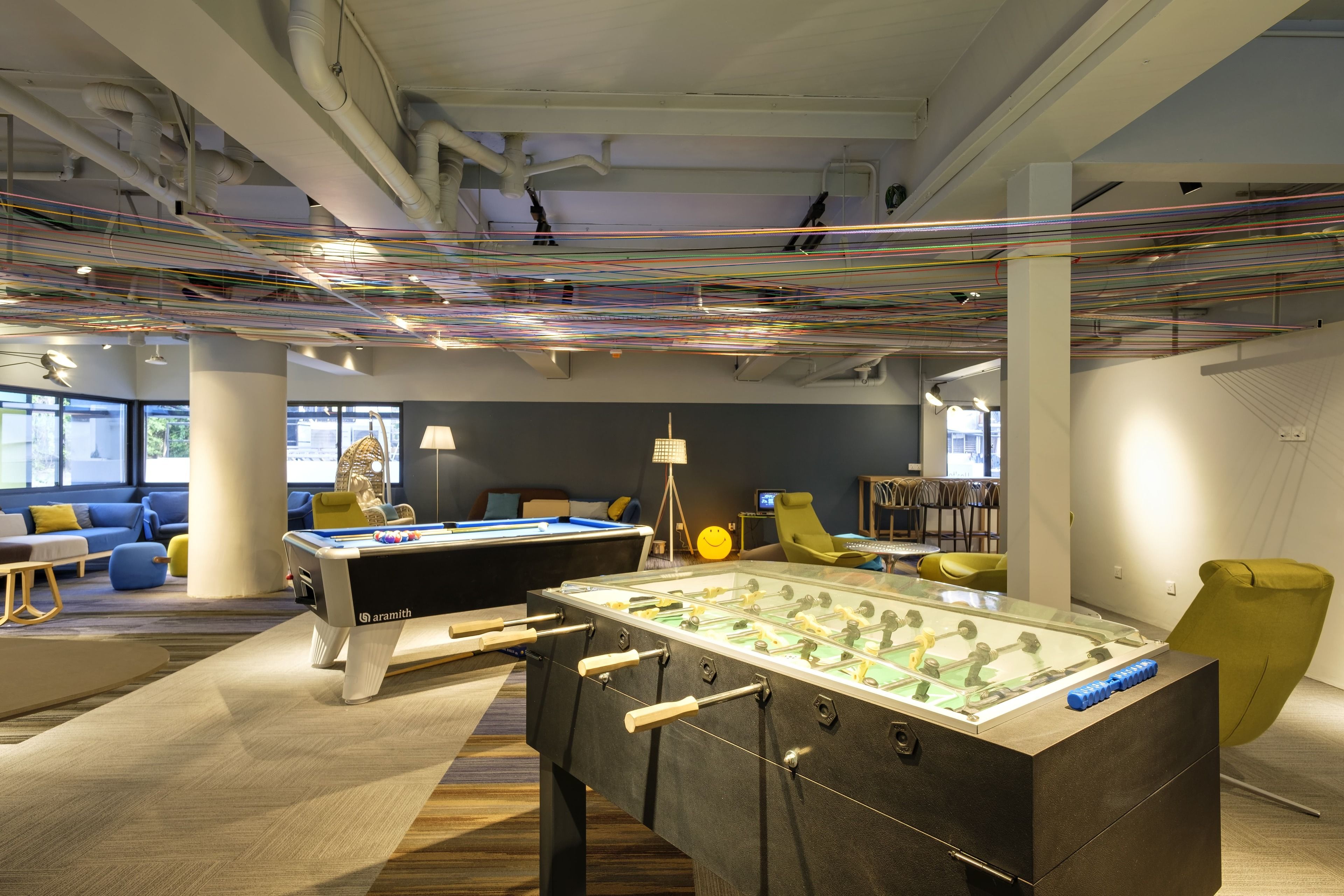 A modern indoor space with two foosball tables, a sofa, and a lamp.