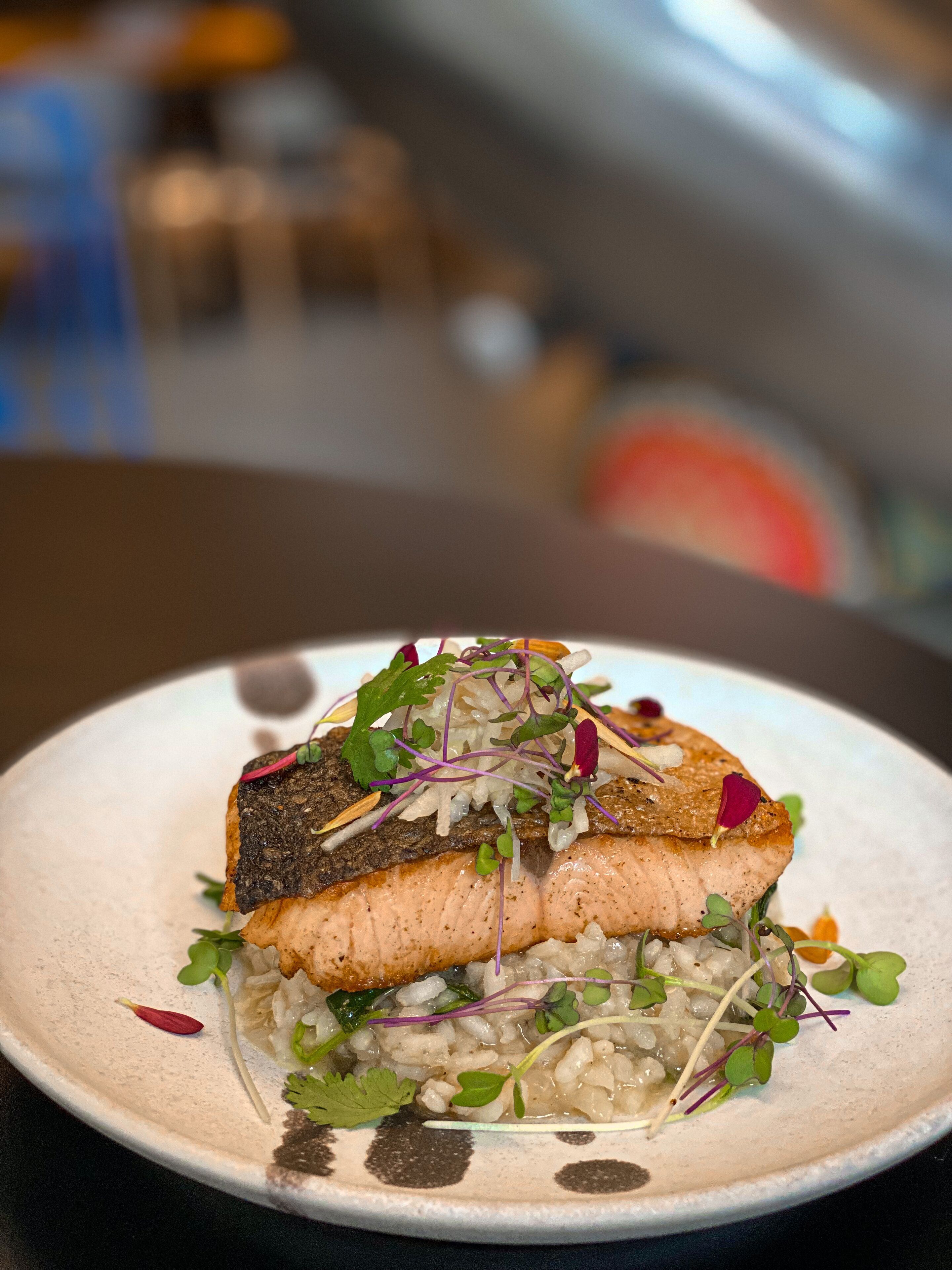 A plate with a piece of fish, greens, and grains.