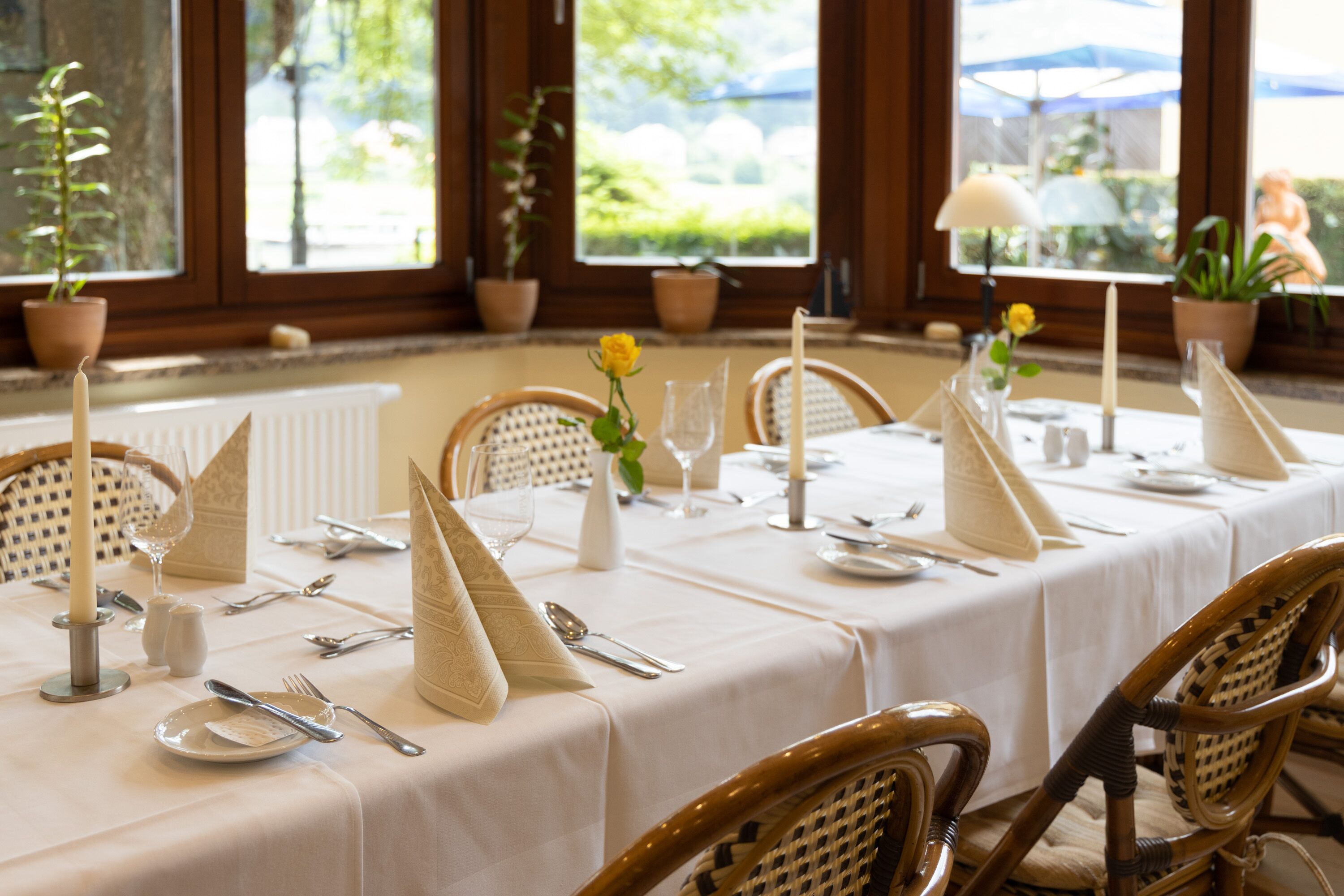 A dining table set with white tablecloth, candles, and wicker chairs.