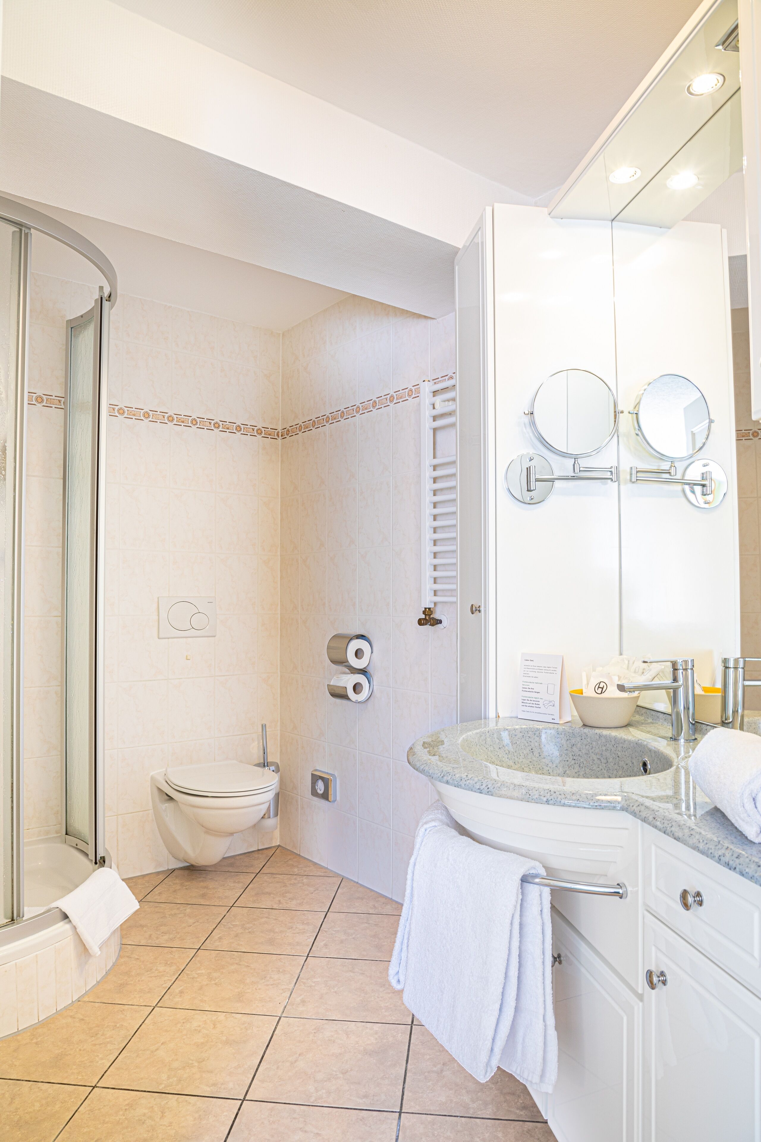 Un baño moderno con cabina de ducha de vidrio, inodoro, lavabo con espejo y barra para toallas.