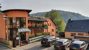 Ett hotell med en modern fasad, en balkong med blomlådor och en parkeringsplats med flera bilar.