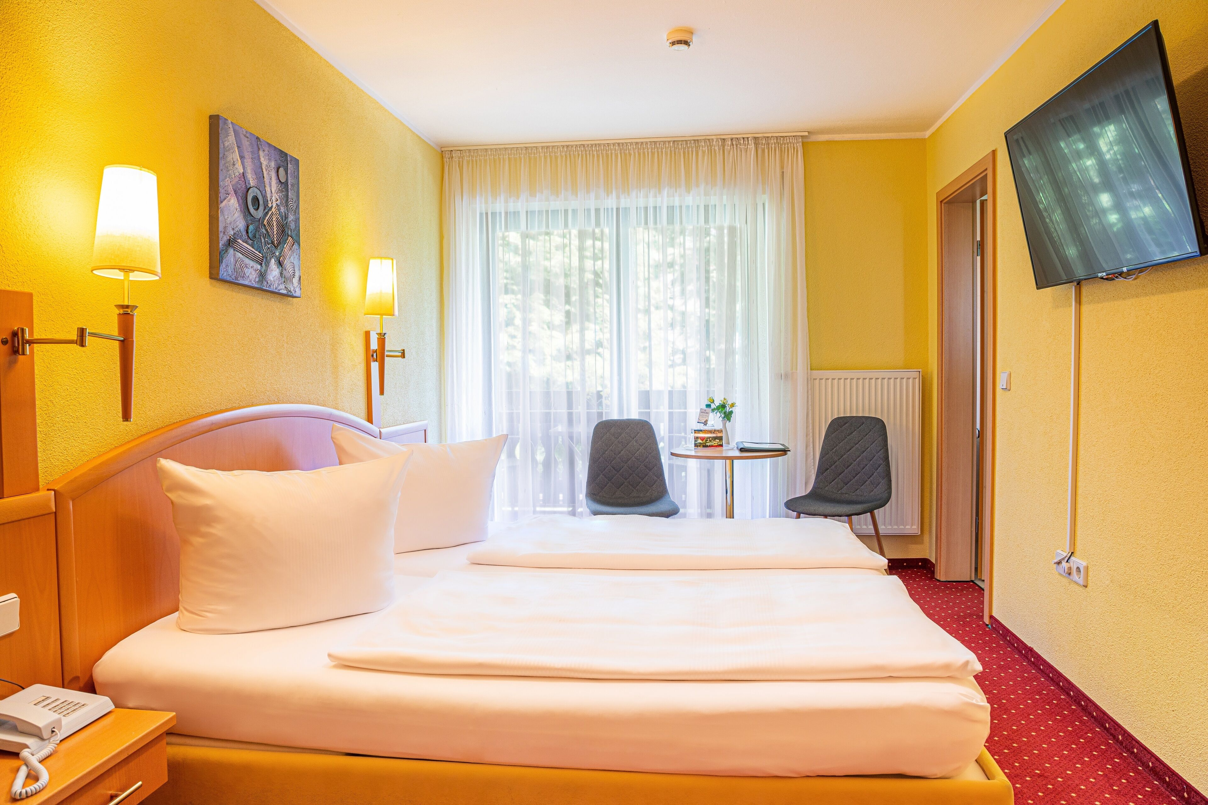Una camera d'albergo con un letto, due abat-jour, una TV, una sedia e un tavolino.