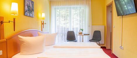Una camera d'albergo con un letto, due abat-jour, una TV, una sedia e un tavolino.