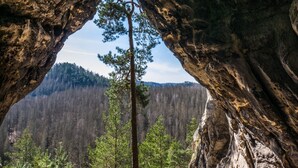 En naturlig klippformation i form av en båge, med utsikt över ett skogbeklätt bergsmassiv.