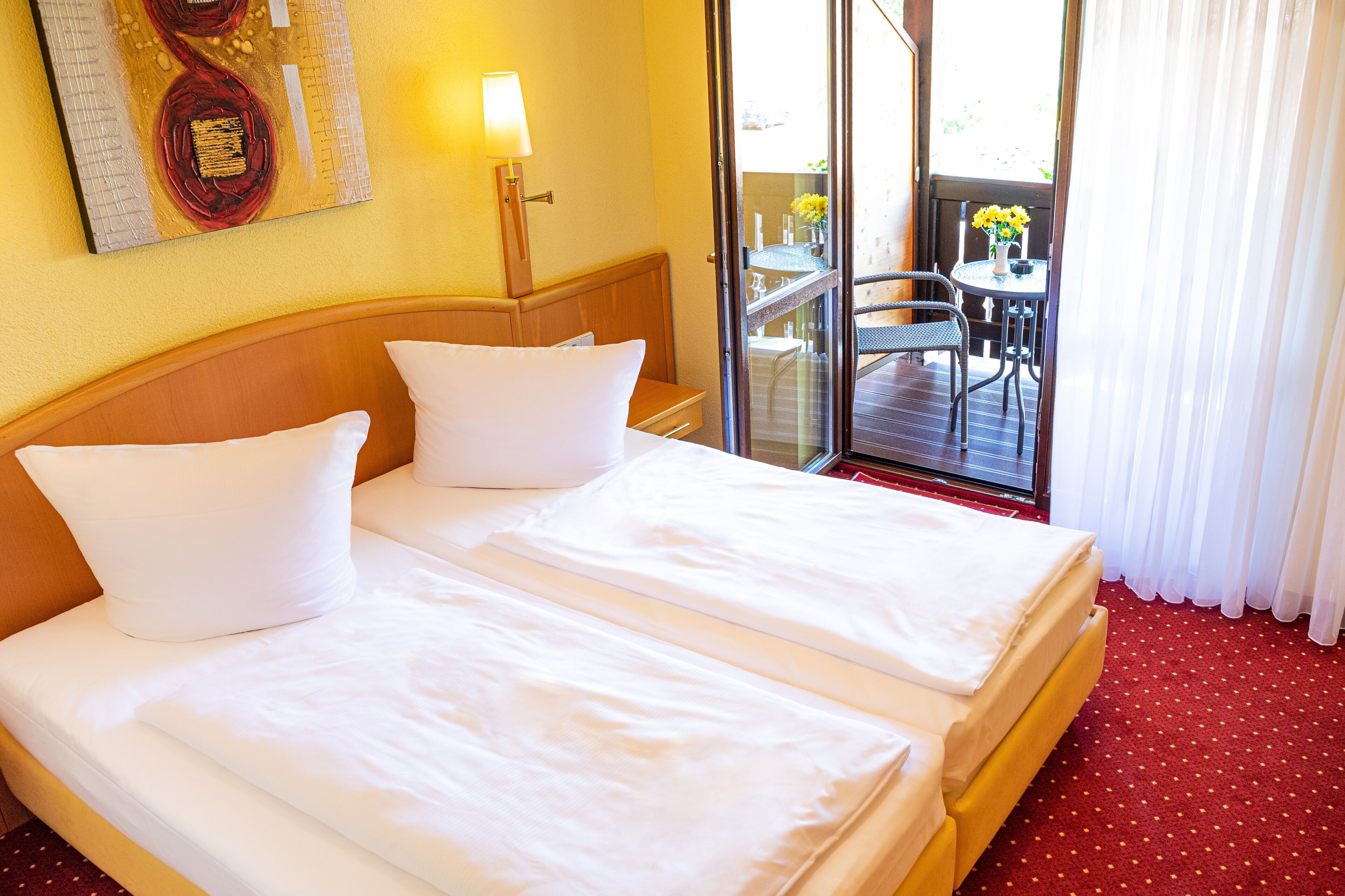 Habitación de hotel con dos camas, un balcón con mesa y sillas, y un cuadro en la pared.