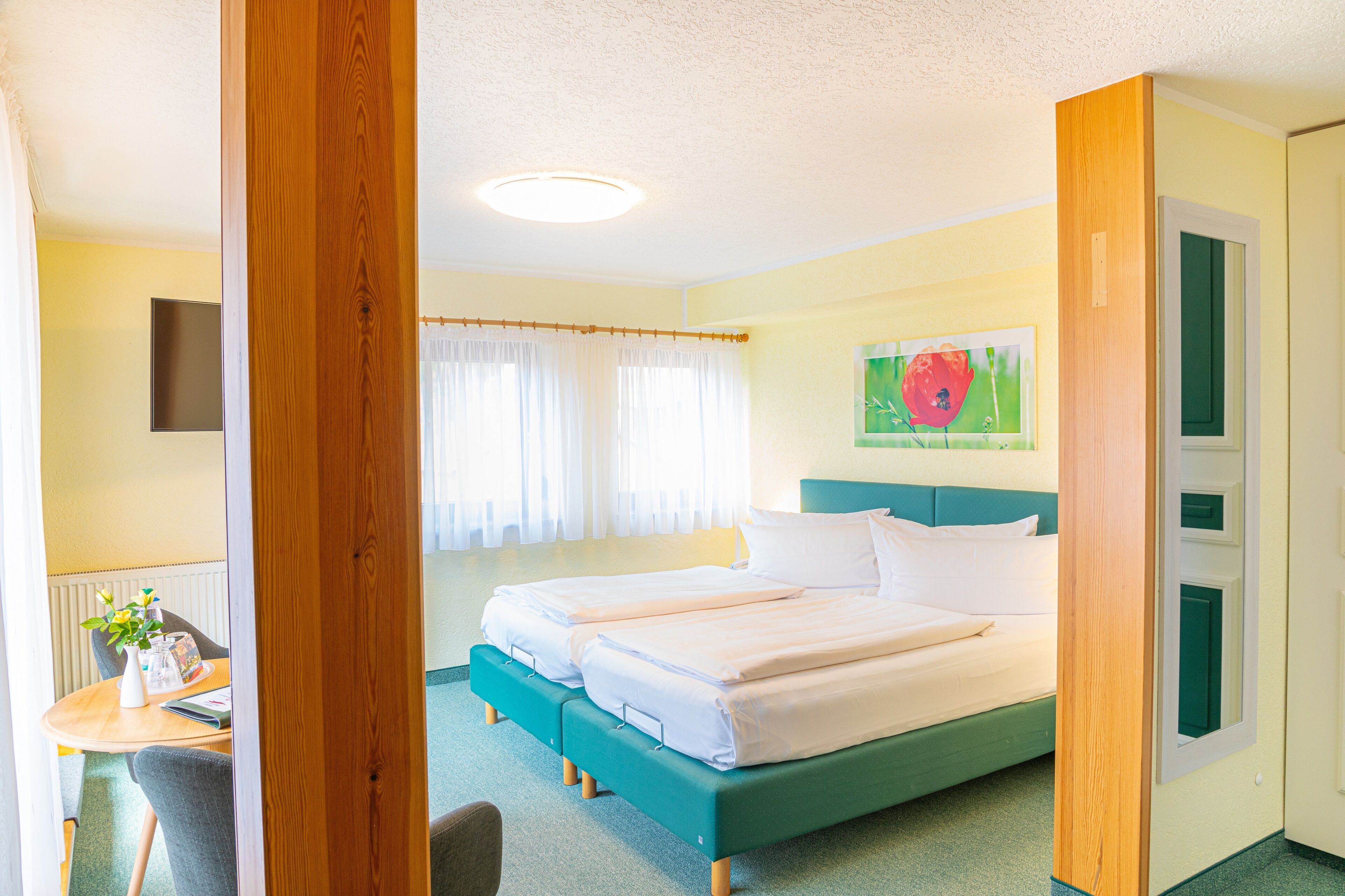 Habitación de hotel con dos camas, un escritorio con silla, una ventana con cortinas y un cuadro en la pared.