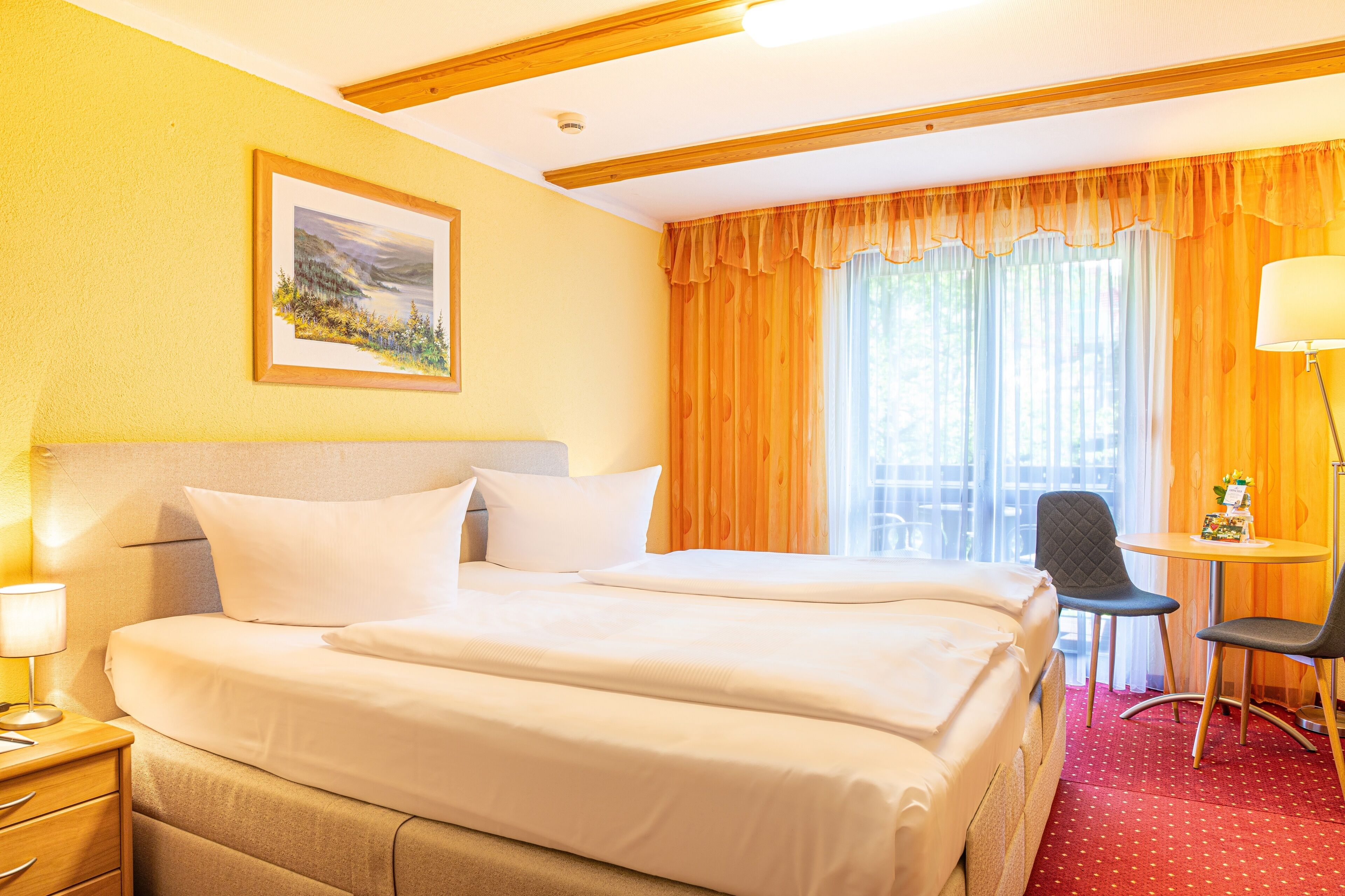 Habitación de hotel con dos camas, un escritorio, una silla y un ventanal con cortinas.