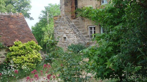 A rustic stone building with a red-tiled roof, surrounded by lush greenery and flowering plants. - La Tour (Marcilly-la-Gueurce)