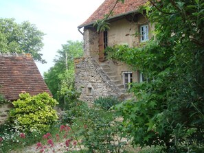 A rustic stone building with a red-tiled roof, surrounded by lush greenery and flowering plants. - La Tour (Marcilly-la-Gueurce)