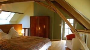 A bedroom with a large bed, a wardrobe, a small white chair, and a skylight. - La Tour (Marcilly-la-Gueurce)