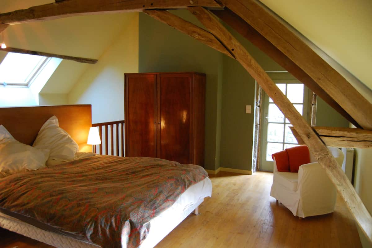 A bedroom with a large bed, a wardrobe, a small white chair, and a skylight.
