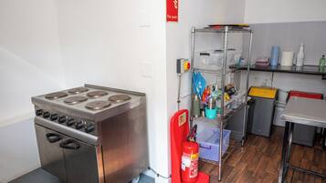 A kitchen with a stainless steel stove, a fire extinguisher, and a metal shelf with various items.