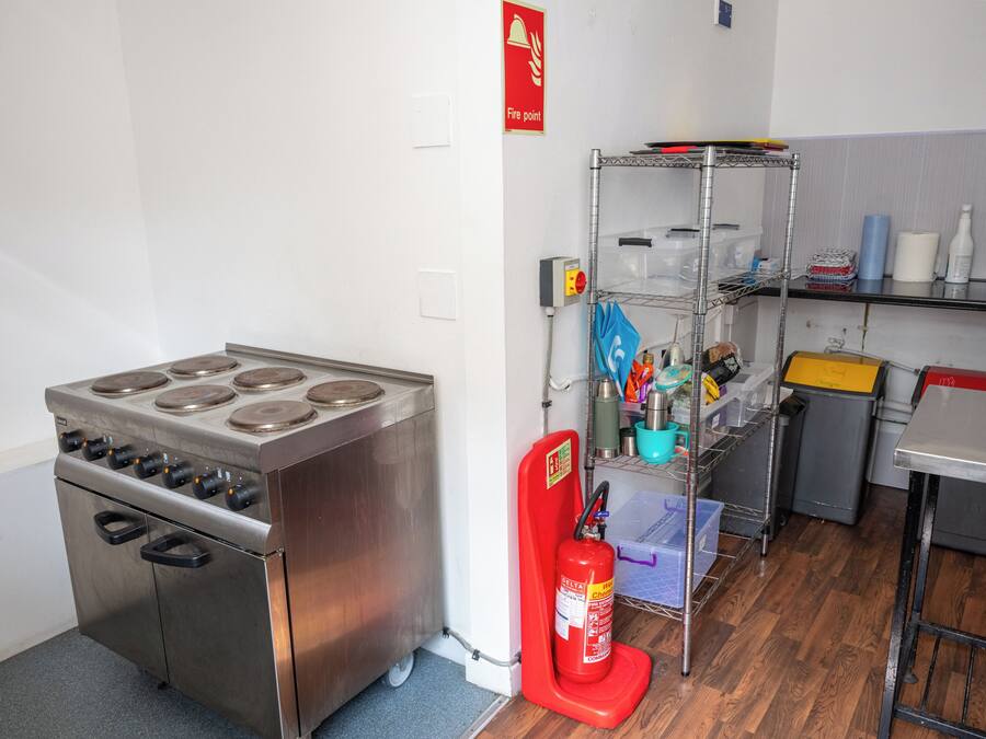 A kitchen with a stainless steel stove, a fire extinguisher, and a metal shelf with various items.