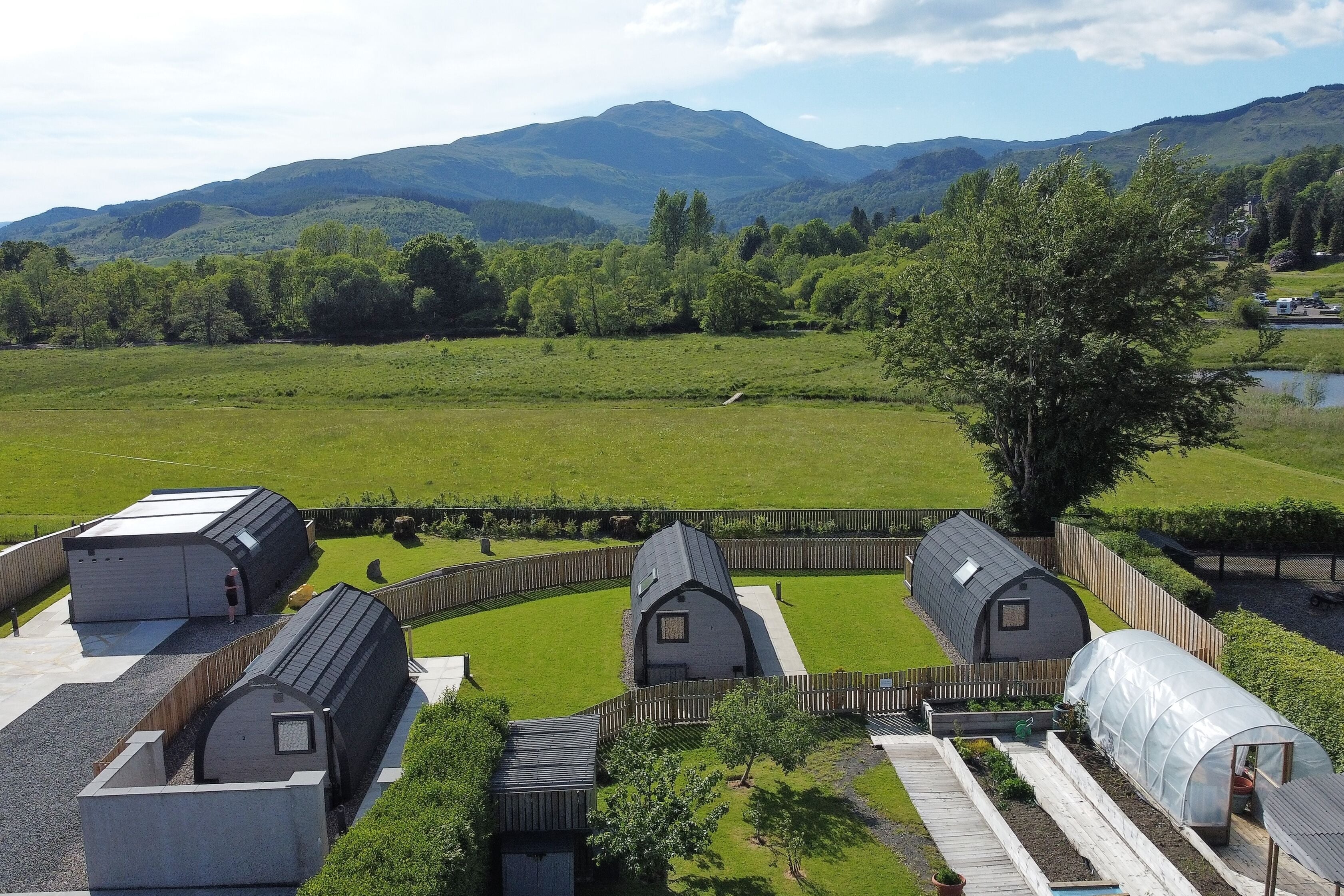 A rural property with multiple greenhouses, a fenced area, and a view of distant hills.