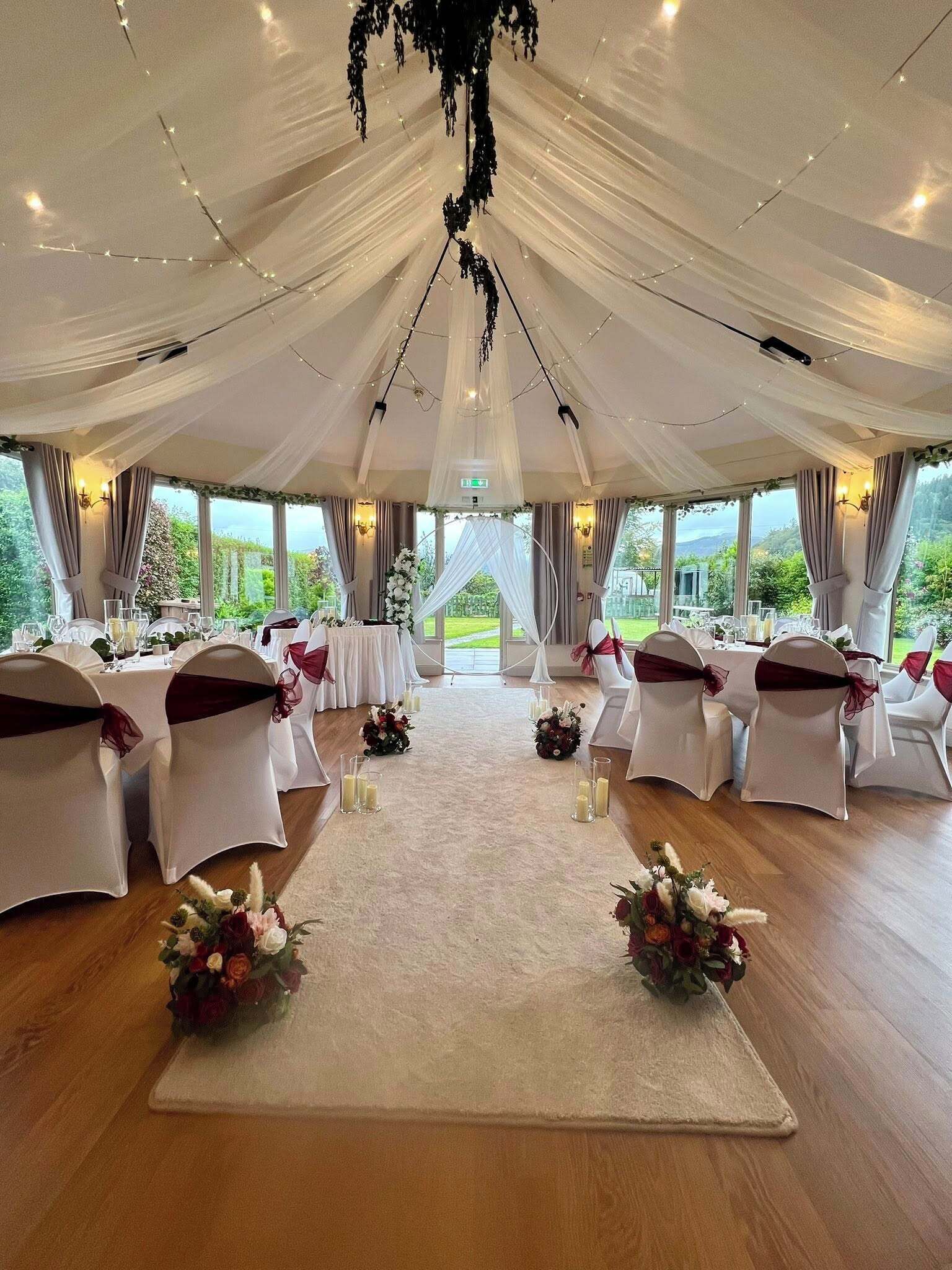 A tented wedding venue with tables and chairs, floral centerpieces, and a view of greenery outside.