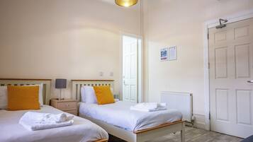 Habitación de hotel con dos camas, una mesita de noche con lámpara, un radiador y una puerta con letrero de salida de emergencia.