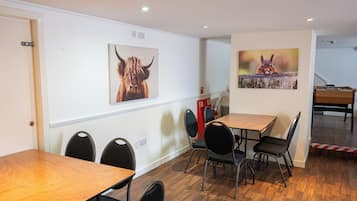 Un comedor con mesas y sillas de madera, dos cuadros en la pared con motivos de animales y un extintor.