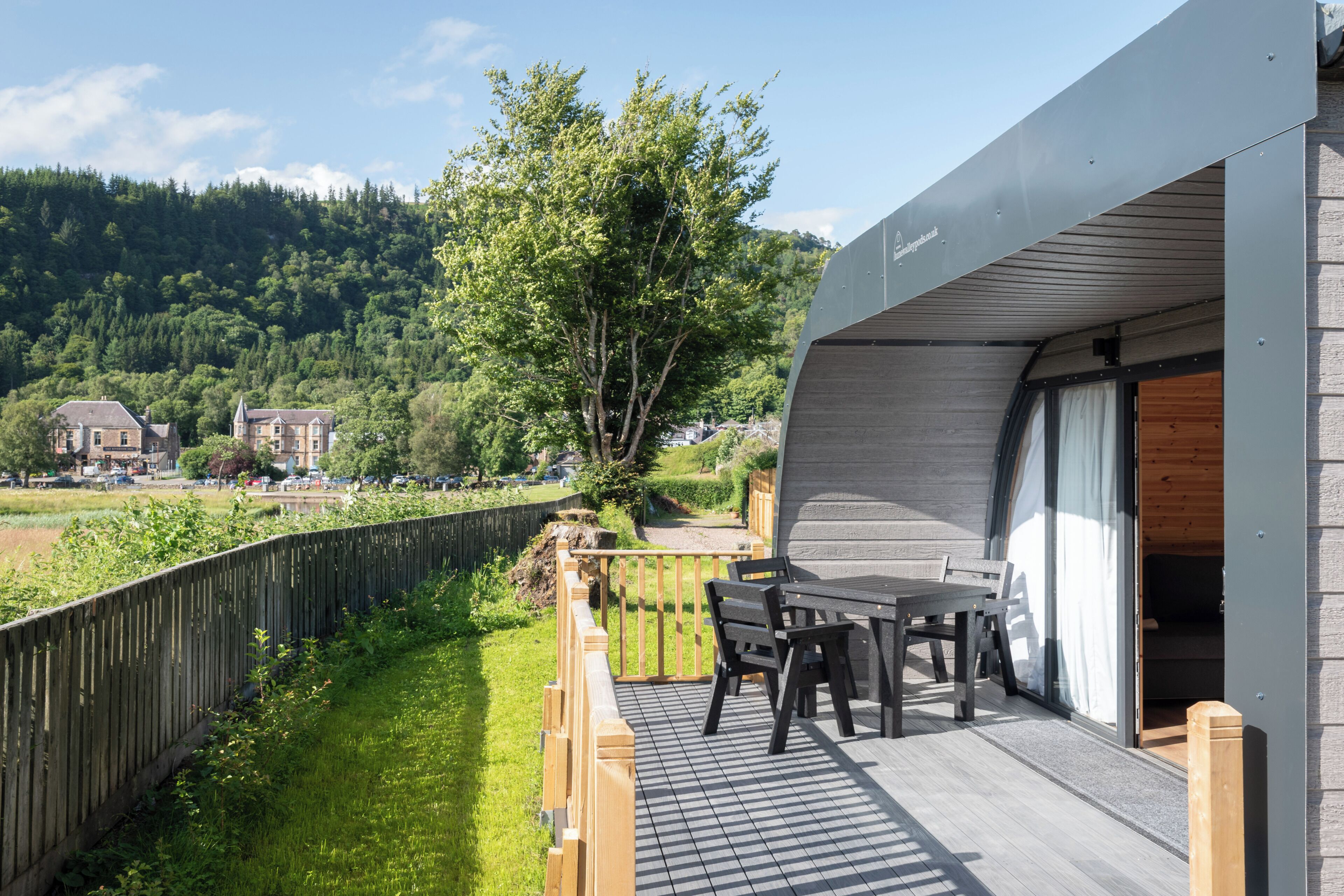 Un balcon avec une table et des chaises, donnant sur une pelouse et une colline boisée.