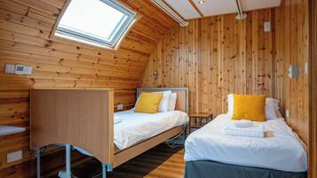 Una habitación tipo cabaña de madera con dos camas, una ventana y un tragaluz.