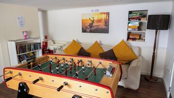 A room with a foosball table, a sofa with cushions, a bookshelf, and a painting on the wall.