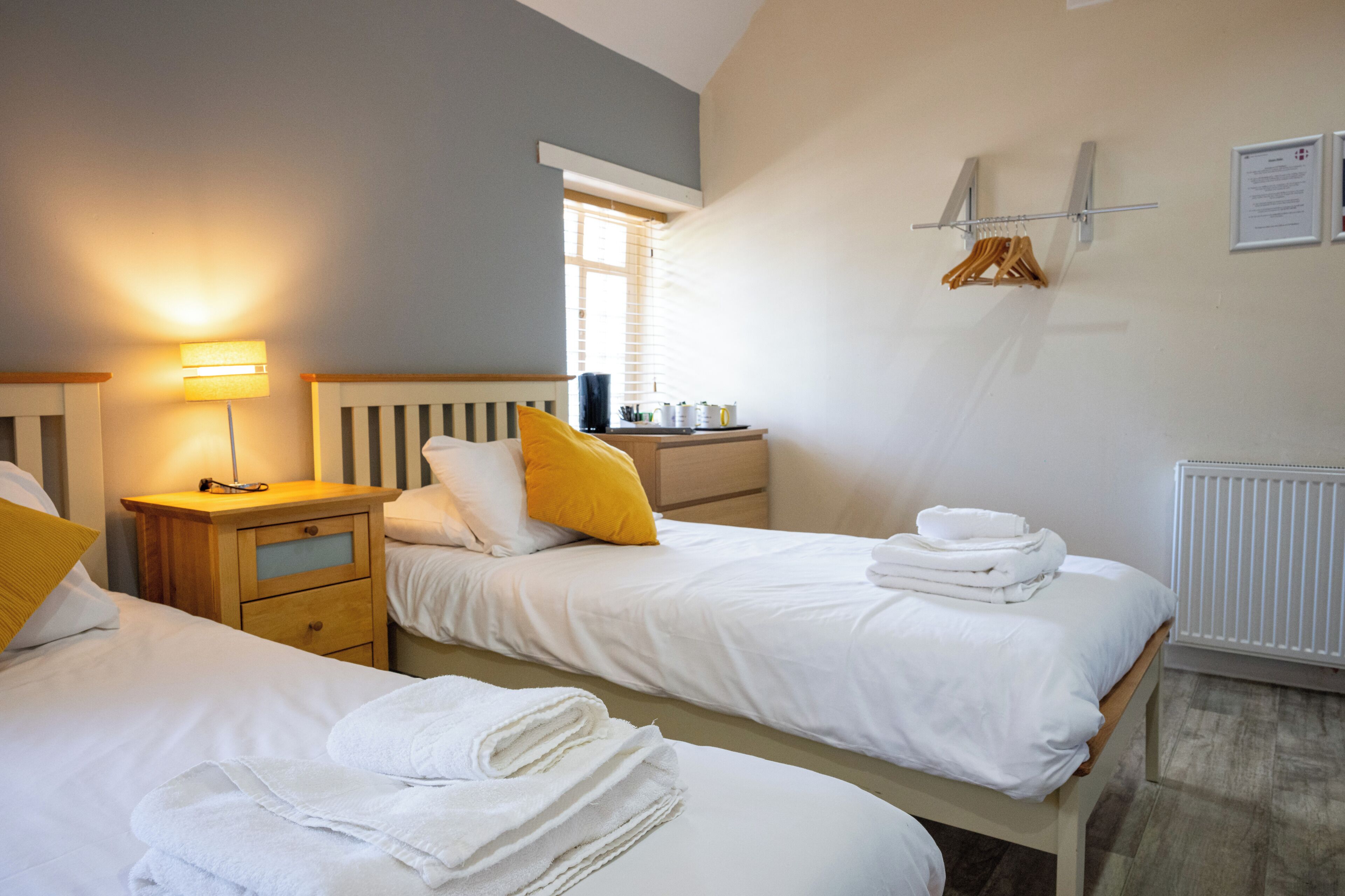 Ein Hotelzimmer mit zwei Betten, einem Nachttisch, einer Lampe und einem Fenster.