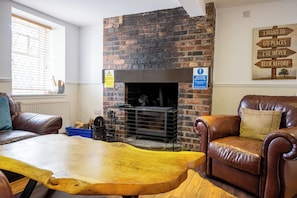 A cozy room with a brick fireplace, leather furniture, and a wooden table. - Callander Hostel (Callander)