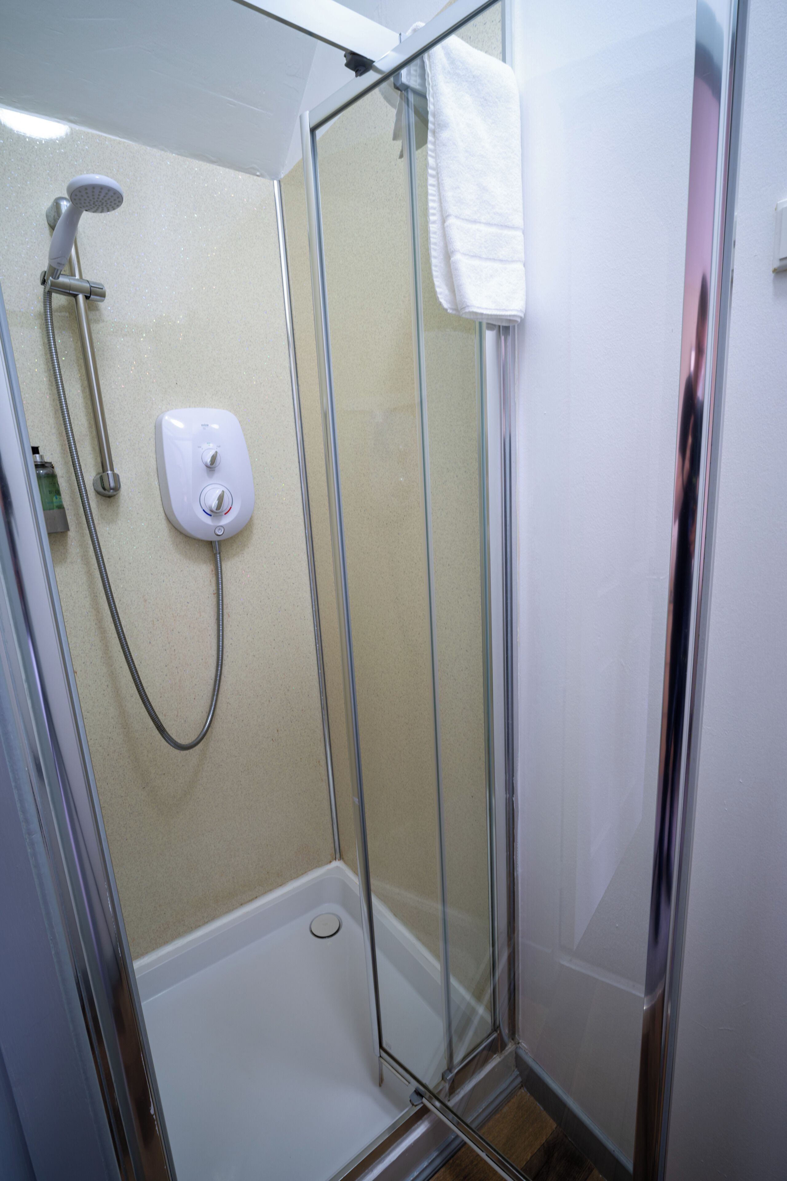 A glass-enclosed shower stall with a handheld showerhead, a control panel, and a white towel hanging on the door.