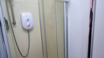 A glass-enclosed shower stall with a handheld showerhead, a control panel, and a white towel hanging on the door.