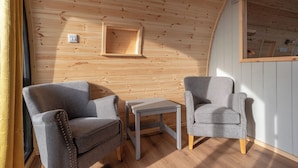 A cozy room with wooden walls, two grey armchairs, a small table, and a window with curtains. - Callander Hostel (Callander)