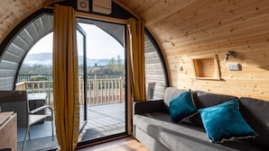 A cozy cabin interior with a curved ceiling, a sofa with cushions, a wooden wall, and a view of the outdoors through a large window. - Callander Hostel (Callander)