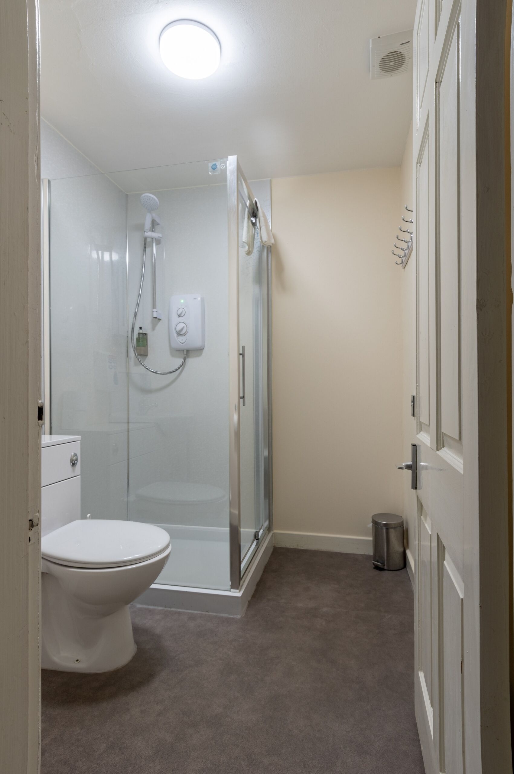 A bathroom with a toilet, a shower enclosure, and a trash can.