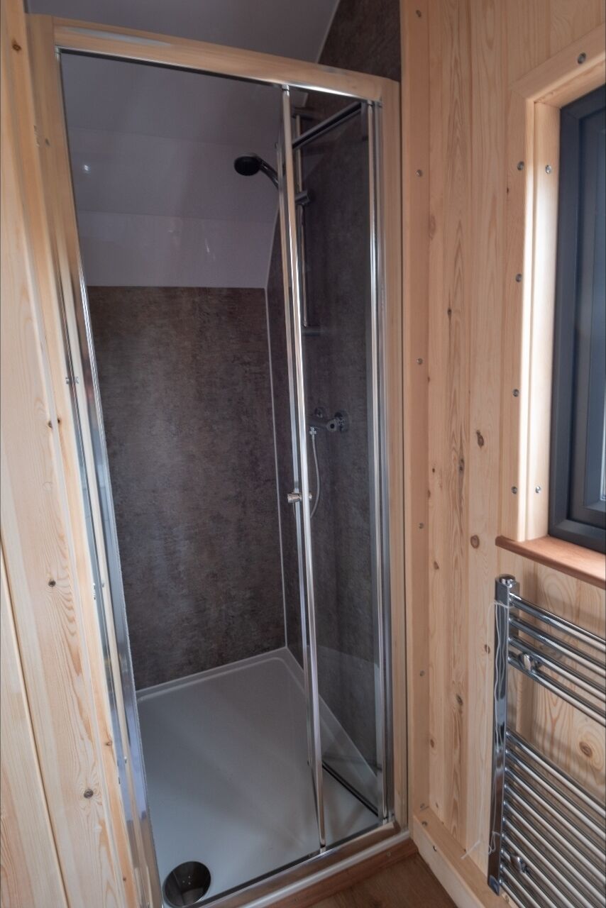 A glass-enclosed shower stall with a wooden frame and a metal showerhead.