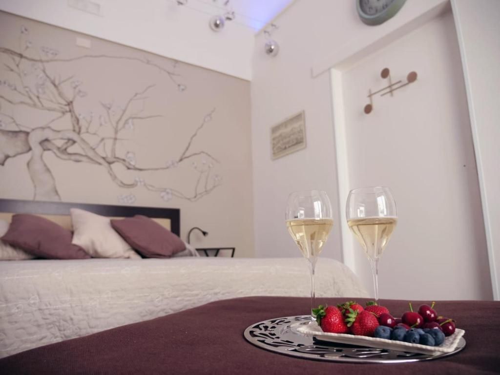 Un dormitorio con cama, un muro con un dibujo de un árbol, dos copas de vino blanco y un plato de fresas y arándanos.