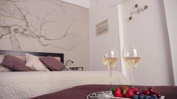 Un dormitorio con cama, un muro con un dibujo de un árbol, dos copas de vino blanco y un plato de fresas y arándanos.
