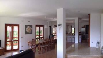 A spacious living area with a dining table and chairs, a sofa, and a kitchen area visible in the background.