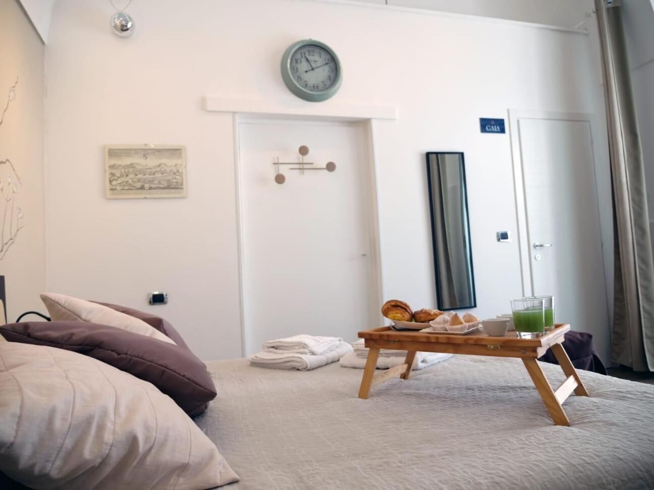 A hotel room with a bed, a bedside table with breakfast items, a clock, and a door with a sign.