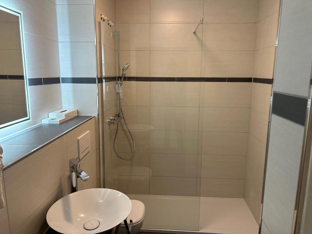 A modern bathroom with a glass-enclosed shower, a white sink, and a toilet.
