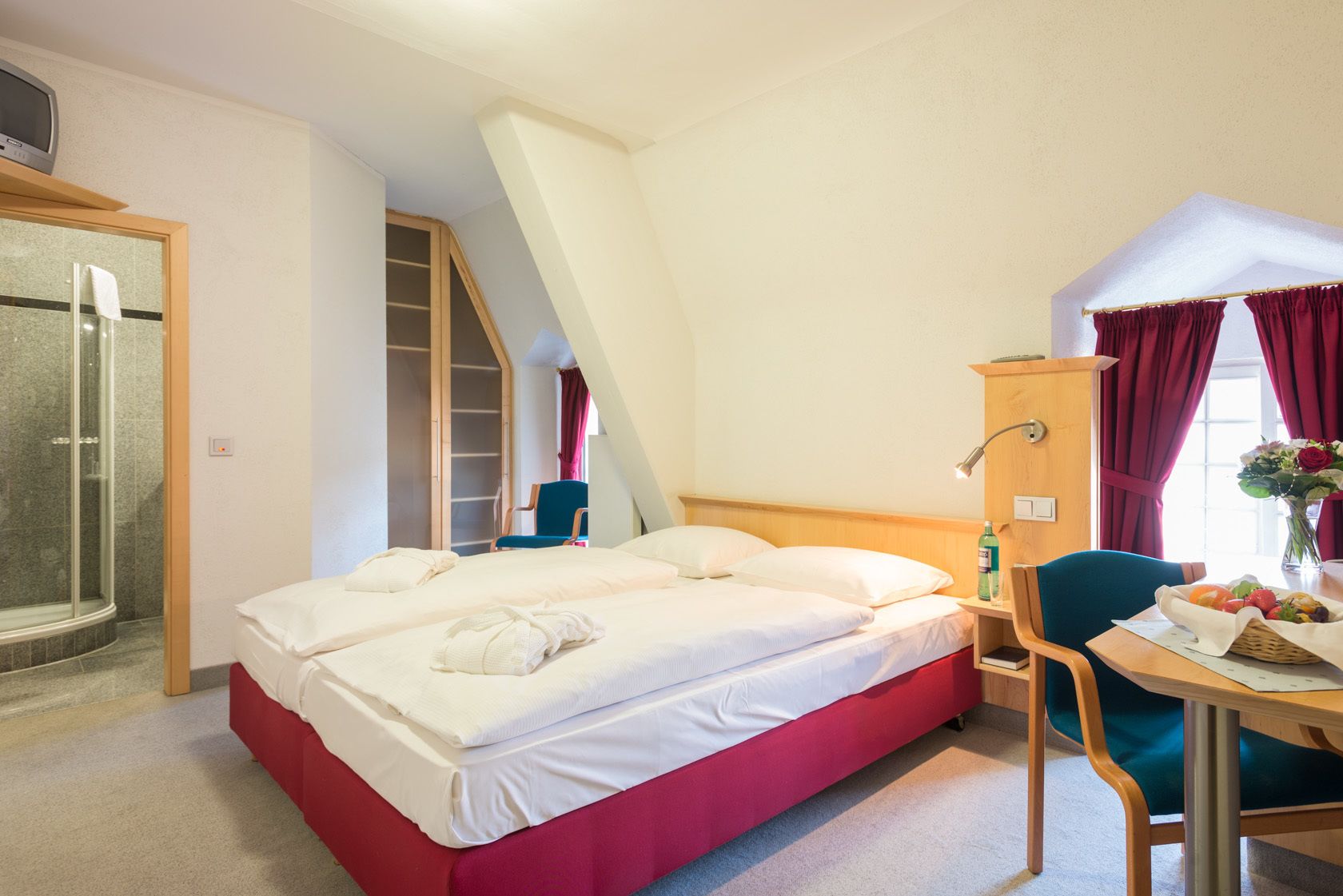 A hotel room with a bed, a desk, a chair, a shower, and a wardrobe.
