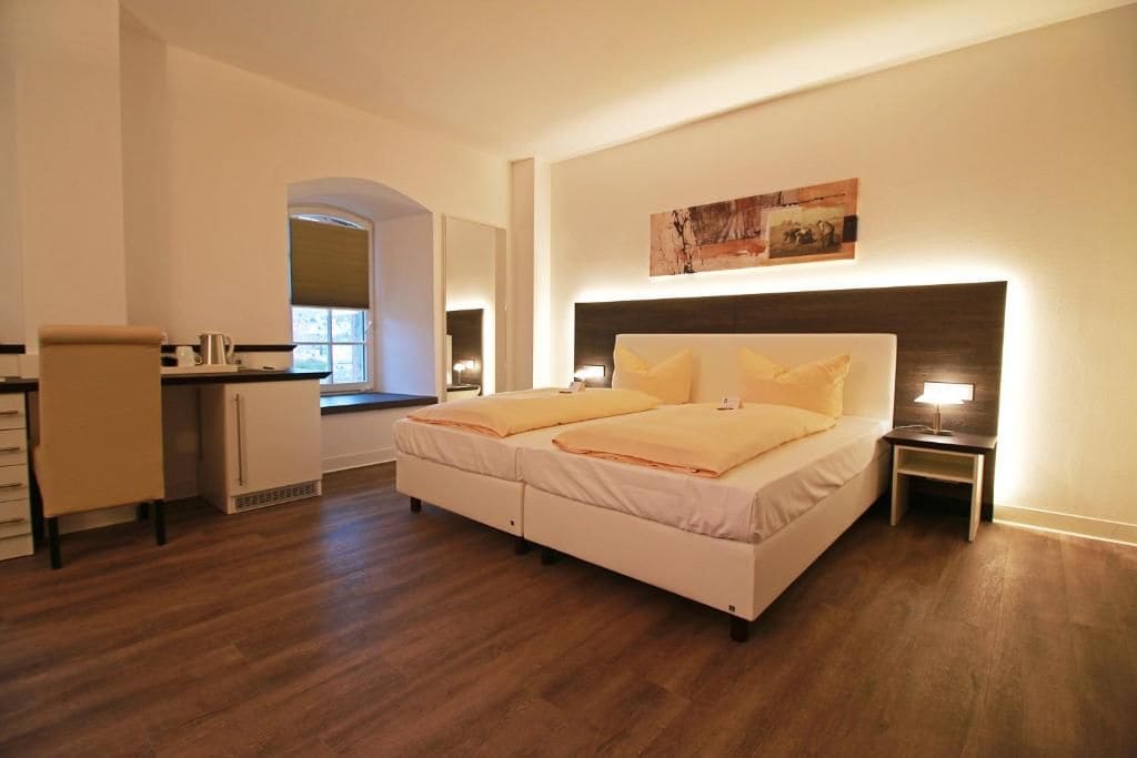 Un dormitorio con cama, mesitas de noche, un escritorio y una ventana.