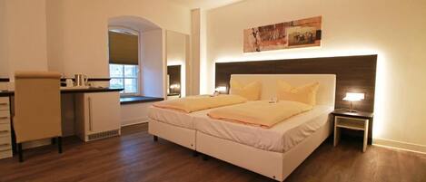 Un dormitorio con cama, mesitas de noche, un escritorio y una ventana.