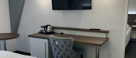 A hotel room with a bed, a desk with a chair, a television, and a coffee maker.