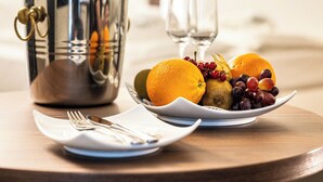 Un desayuno con un plato de fruta, una cafetera y un vaso de agua sobre una mesa de madera.